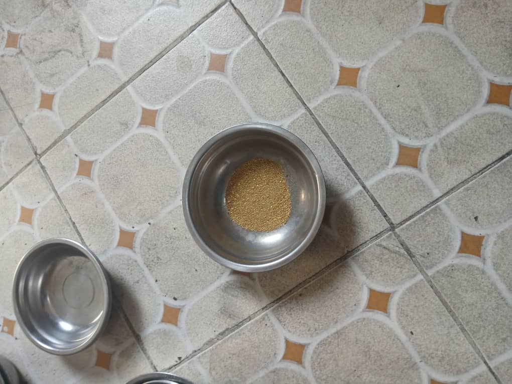 Fine gold dust filling the base of a stainless pan on a tiled floor
