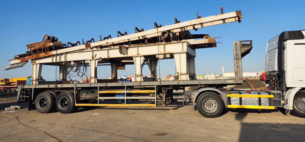 Long conveyor structure loaded on a flatbed trailer behind a prime mover