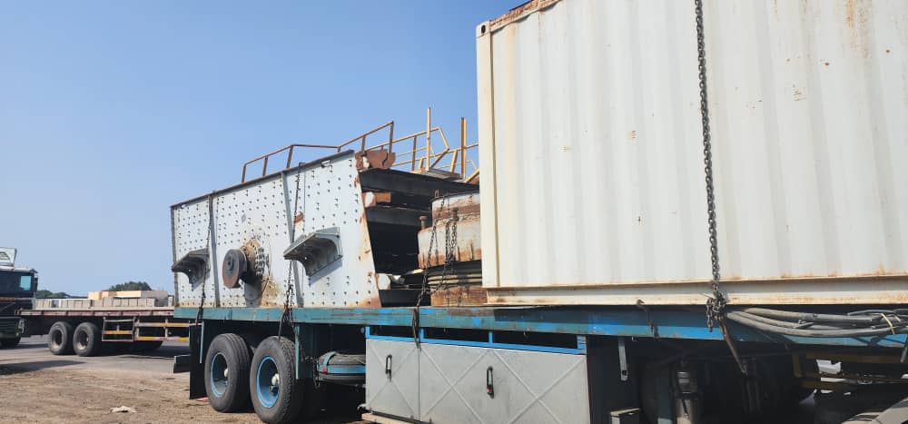 Vibrating screen unit chained to a flatbed trailer next to a shipping container